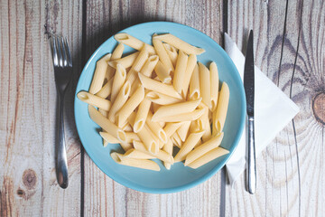 Penne pasta food served on a blue plate on a wooden table close up still