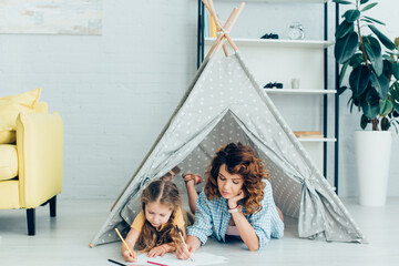 young nanny and cute kid drawing together while lying in toy wigwam © LIGHTFIELD STUDIOS
