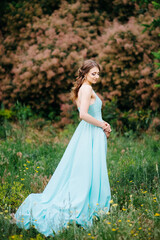 Happy girl in a turquoise long dress in a green park