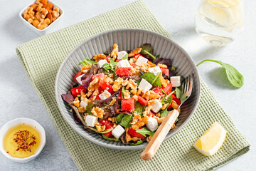 Summer refreshing salad with watermelon, feta cheese, walnuts and greens on concrete table top with lemon water, top view. Recipe for heat wave