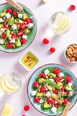 Light salad with raspberry, baby spinach, feta cheese, avocado and walnuts, top view. Fresh original summer salad with lemon water on pink table top, copy space, vertical image