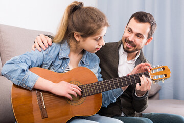 happy russian male tutor assisting teenage pupil in learning how to play guitar