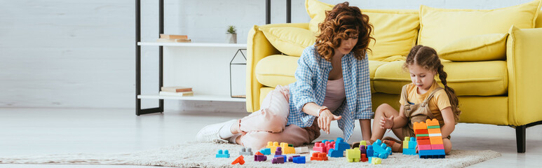 horizontal concept of babysitter and cute kid playing with multicolored building blocks on floor