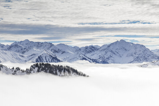 Snow covered mountains with inversion valley fog and trees shrouded in mist. Scenic snowy winter landscape in Alps, Allgau, Kleinwalsertal, Bavaria, Germany.
