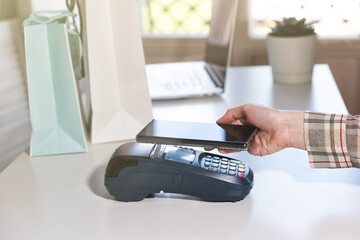 Woman pay by phone. NFC payment terminal on a white table. Credit card or phone pay pos banking device, card machine.