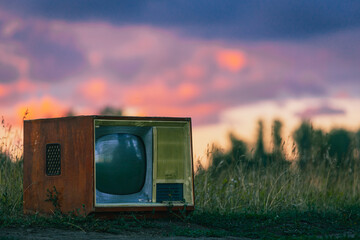old retro TV set on a field road against a wheat background under the rays of the setting sun