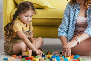 cropped view of babysitter and adorable kid playing on floor with multicolored blocks