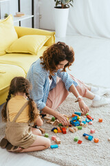 high angle view of child with babysitter playing with multicolored cubes on floor