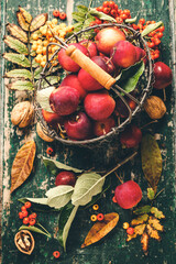 Apples in basket and autumn decorations on old wooden background