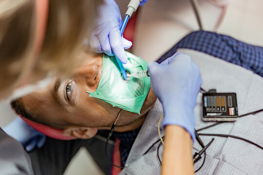 Patient with a kofferdam is being treated by a dentist.Dentist performs dental treatment by putting an injection to a smiling patient.