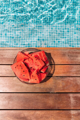 Round plate with watermelons near the pool on the plank floor. Summer concept. 