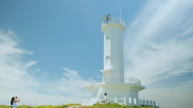 A woman taking pictures of the blue sky and white lighthouse. Jeju Island.