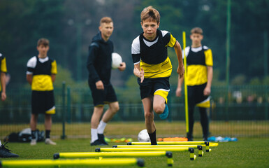 Boys on football training session with two young coaches. Junior level soccer player running and...