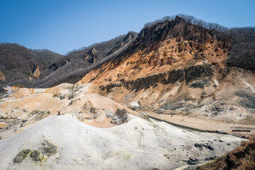 Fototapeta na wymiar Beautiful view of Noboribetsu Jigokudani or Hell Valley in sunny day with blue sky in background. Autumn season and sulfur gas steaming out from ground.