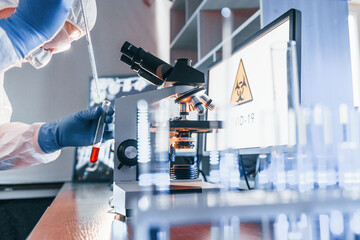 Scientist in white protective uniform works with coronavirus and blood tubes in laboratory
