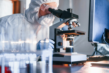 Monitors with information on the table. Scientist in white protective uniform works with coronavirus and blood tubes in laboratory