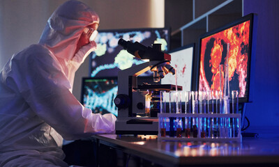 Monitors with information on the table. Scientist in white protective uniform works with coronavirus and blood tubes in laboratory