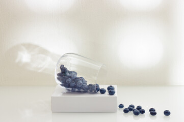Blueberries in a glass on a white background with shadows on the wall. Vegetarian and organic food concept.