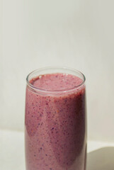Blueberry pink smoothie in a transparent glass on light background with long shadows, top view. Milk Shakes. Healthy breakfast. Healthy food and vitamins concept