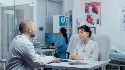 Obraz premium Young woman receiving some good news at the doctor after consulting the X Ray, she smiles and is happy.