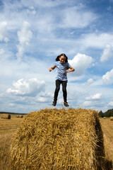 The girl jumps high into the air on a roll of hay against a blue sky and a shoe. shows hanging face, tongue