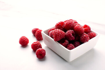 Сloseup of pile of ripe raspberries, white square bowl full of juicy raspberries