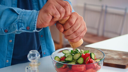 Man pouring salt over healthy salad in kitchen for delicious meal. Cooking preparing healthy organic food happy together lifestyle. Cheerful meal in family with vegetables