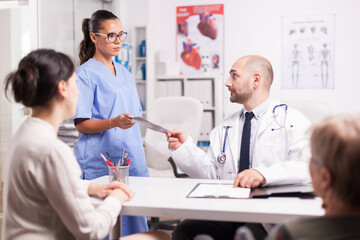 Fototapeta premium Nurse giving doctor patient x-ray during examination in hospital office. Daughter and her disabled mother in wheelchair at periodic medical check. Medic wearing white coat and stethoscope.