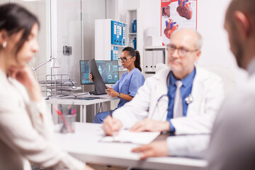 Medical nurse looking at x-ray. Senior doctor wearing white coat and stethoscope during consultation of couple in hospital office. Pair at medical check.