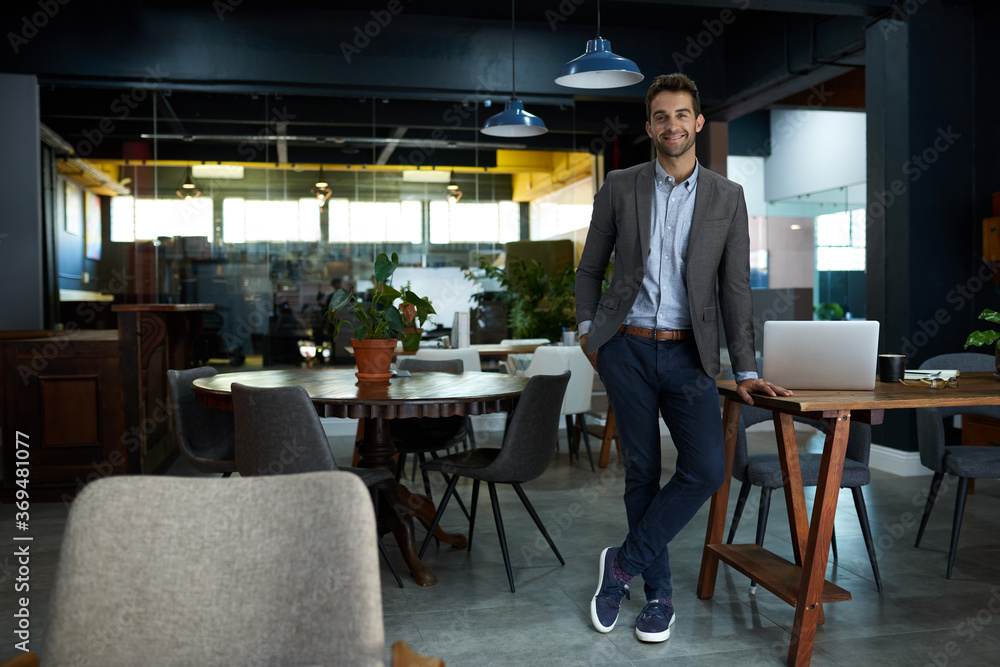 Wall mural Smiling young businessman standing in an office after working hours