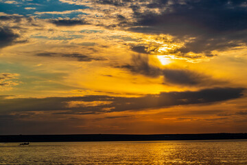 Sunset through the clouds over the water and ship on the water