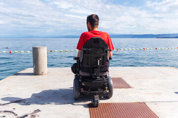 Fototapeta premium Man sitting in a wheelchair on the beach. Dangers of jumping into water from heights. Head and spine injury.