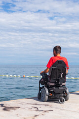 Obraz premium Man sitting in a wheelchair on the beach. Dangers of jumping into water from heights. Head and spine injury.