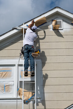 Painter masking off trim at the peak of a house before spraying paint