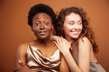 two pretty girls african and caucasian blond posing cheerful together on brown background, etnithity diverse lifestyle people concept