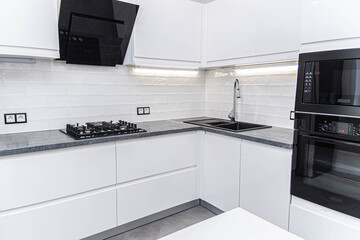 interior of white furniture of a compact kitchen, glossy cabinets with built-in household appliances.