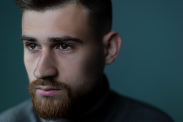 close-up portrait of a young handsome bearded guy looking to the side. A dramatic portrait. psychological, studio portrait on a gray background.