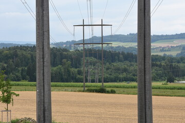 View between two electricity pillars of power transmission tower of high voltage electricity in the middle of meadow to next electrical poles in countryside during sunny day.