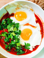 Two fried eggs cooked with tomato sauce and vegetables served with two pieces of homemade bread in white plate for an healthy breakfast