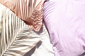 Three pillows white, lavender and peach on the bed. Contrasting shadows with palm leaves