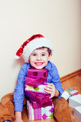 little cute boy with Christmas gifts at home wearing red Santas hat. closeup emotional happy smiling in mess with toys, lifestyle holiday people concept