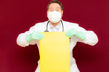 Front view Young handsome doctor holding yellow blank banner. Place your text advertisement.burgundy wall.