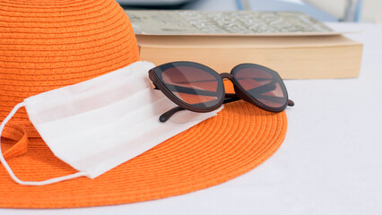 Safe tourism concept: orange summer hat and white medical mask , sun glasses on blue background...