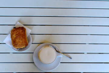 Italian cappuccino with a chocolate croissant on a white slatted table