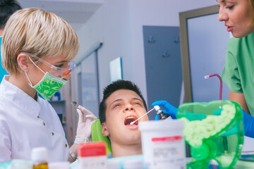 Closeup picture of a female dentist examining teenage boy's teeth in the dental office.