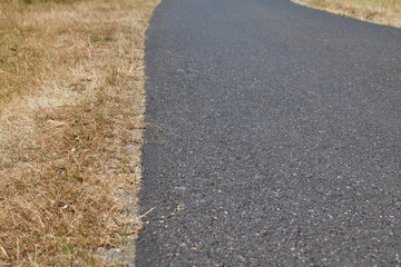 Wąska asfaltowa droga na wsi wraz z trawiastym poboczem spalonym od słońca.