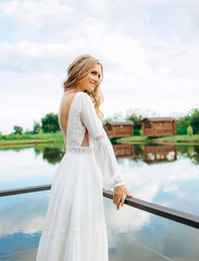 Blonde hair bride in white silk long lace dress standing back on the terrace with lake view