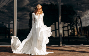 Beautiful blonde waving wedding dress on the background of a modern building