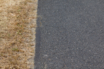 Fragment wąskiej asfaltowej drogi na wsi wraz z trawiastym poboczem spalonym od słońca.