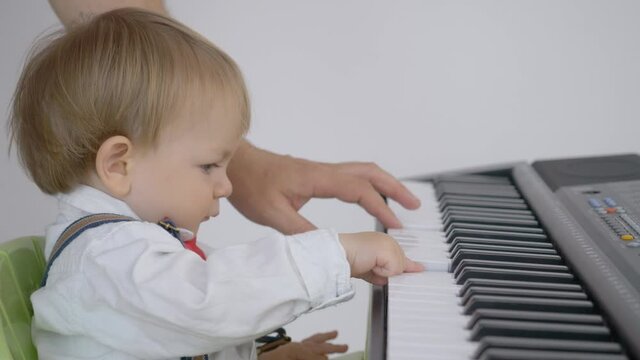 Portrait of little child playing at piano, parent hand teach boy